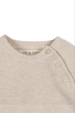 Close-up of a beige, textured sweater romper with button closures, featuring the brand name Hope & Henry on the label.