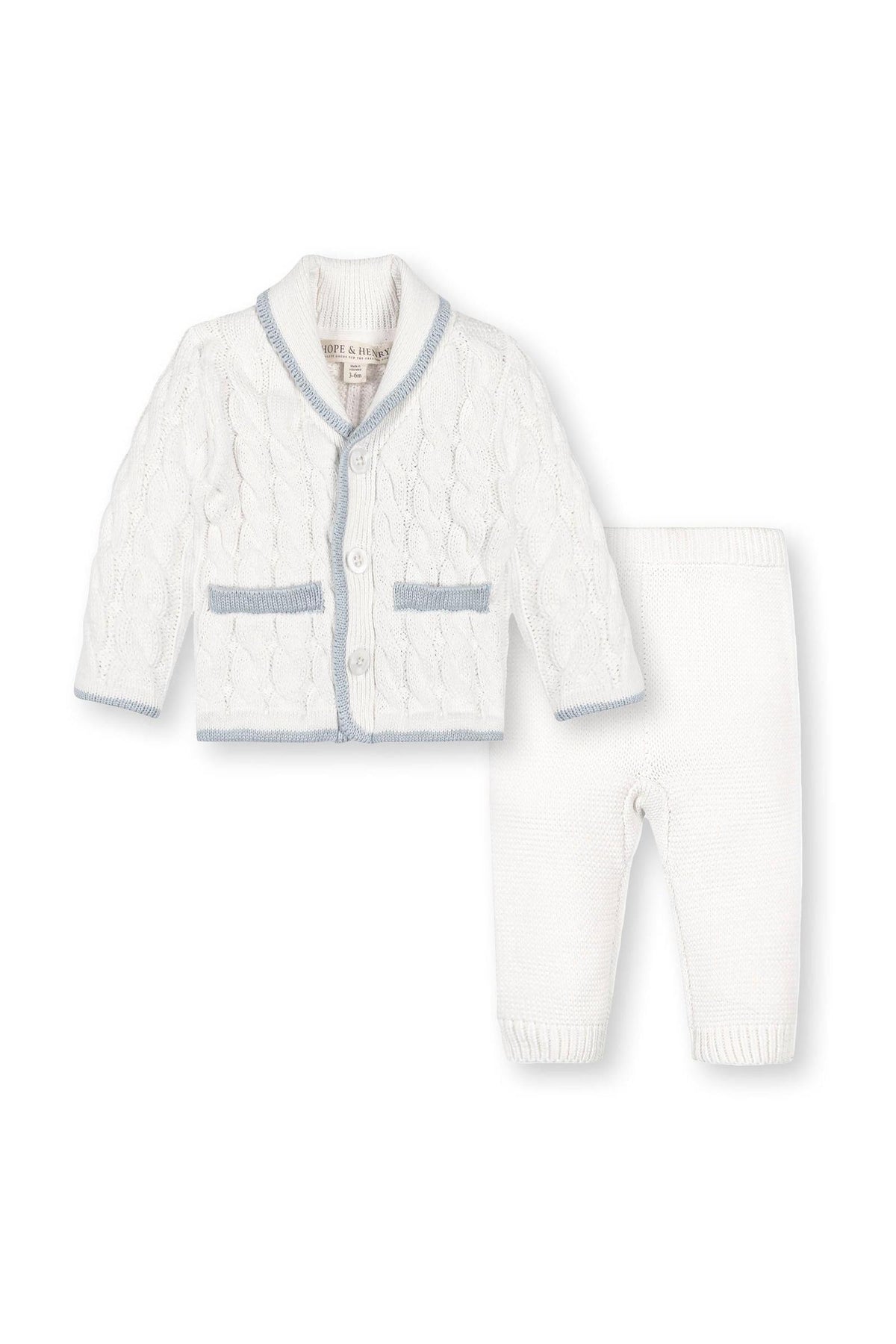 A cozy baby gift set featuring a white cable-knit cardigan with a shawl collar and blue trim, paired with matching white leggings. Made from soft organic cotton for comfort.
