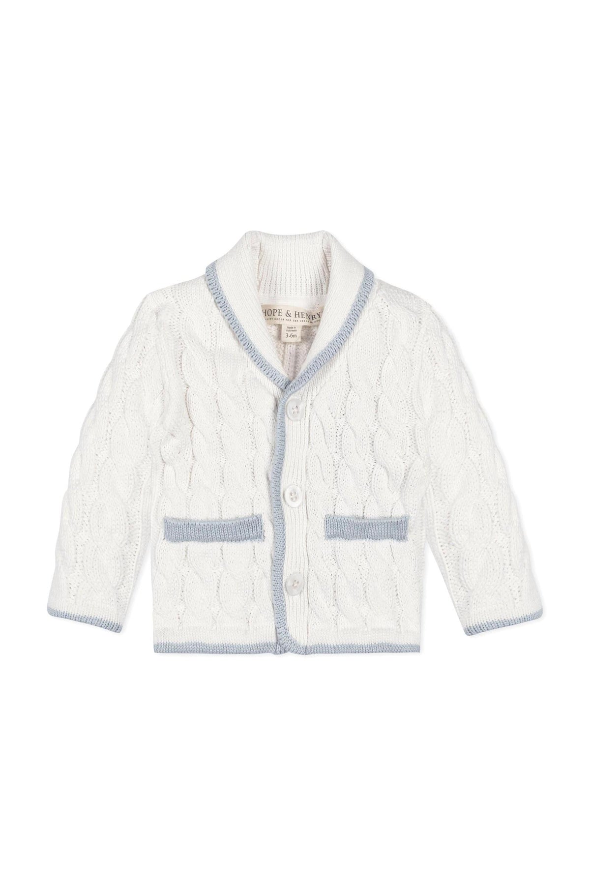 A cozy, white knitted cardigan features a shawl collar and blue accents, perfect for babies. Made from organic cotton, it offers softness and comfort for everyday wear.