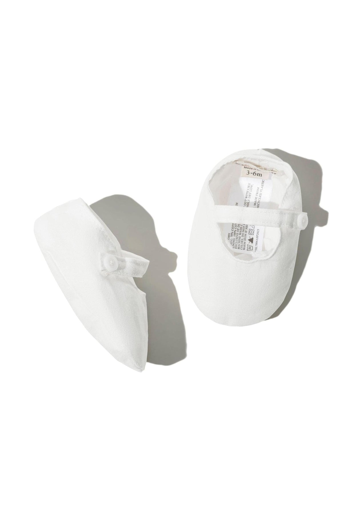White linen baby shoes with a button strap closure, perfect for infants aged 3-6 months, showcasing a soft and stylish.