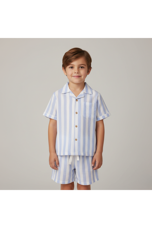 A young boy smiles while wearing a light blue and white striped organic cotton shirt and shorts set. The outfit features a button-down shirt with a pocket, perfect for summer.