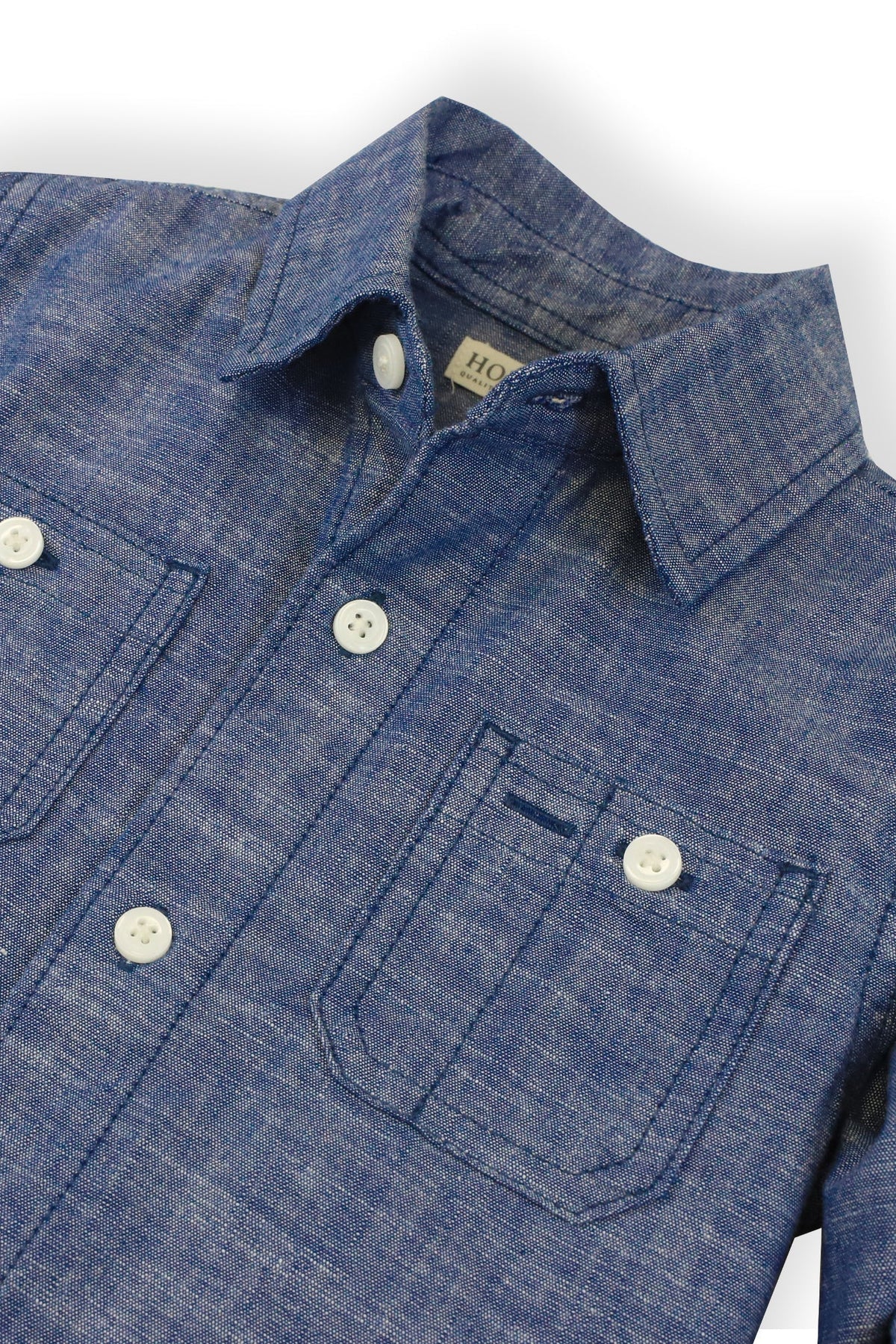 A close-up of a blue chambray shirt made from organic cotton, featuring a button-down collar and two front pockets.