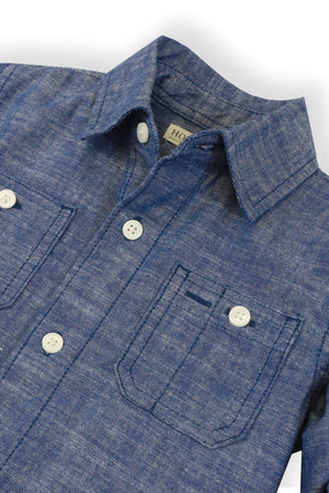 A close-up of a blue chambray shirt made from organic cotton, featuring a button-down collar and two front pockets.