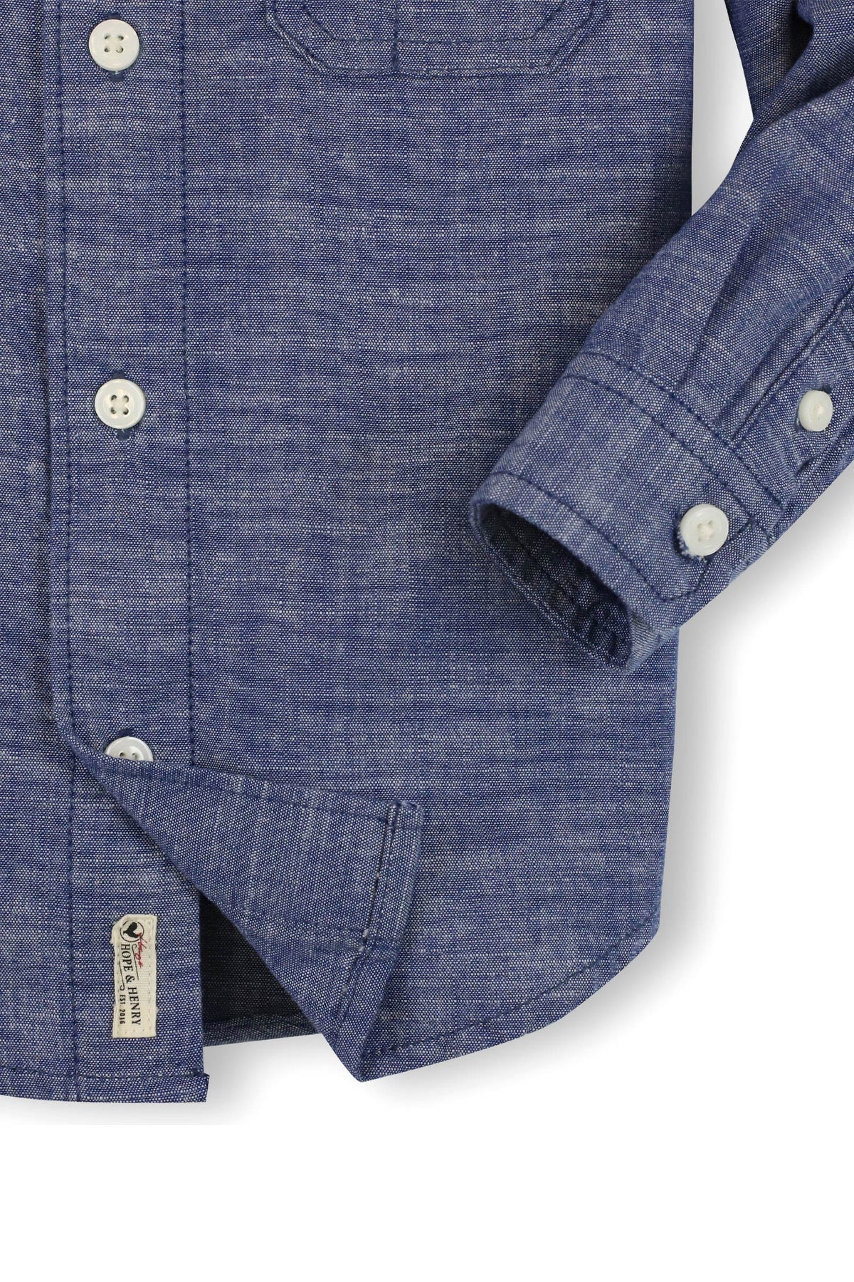 A close-up of a blue chambray button-down shirt made from organic cotton, featuring two chest pockets and white buttons.
