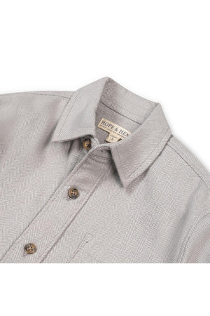 Close-up of a grey organic cotton flannel shirt featuring a herringbone pattern, button details, and a collar. The shirt is from Hope & Henry, designed for ages 2T to 18.