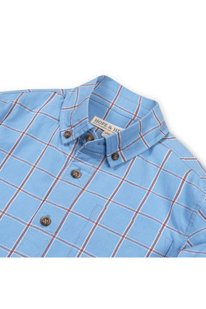 A close-up of a blue plaid shirt featuring a button-up collar and brown buttons. Made from soft organic cotton, this shirt is designed for comfort and classic style.