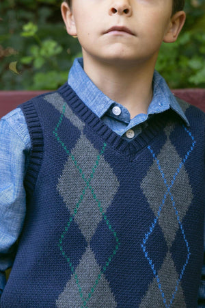 A young boy models a navy and gray argyle sweater vest made from soft organic cotton, layered over a light blue shirt, showcasing a classic, polished look.