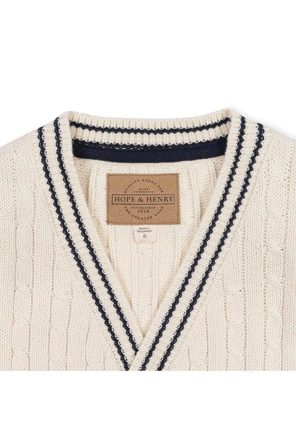 Ivory organic cotton cable cardigan featuring a classic knit design with navy stripes along the collar. The product label reads Hope & Henry, indicating its sustainable and family-friendly attributes.
