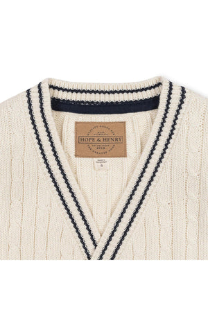 Ivory organic cotton cable cardigan featuring a classic knit design with navy stripes along the collar. The product label reads Hope & Henry, indicating its sustainable and family-friendly attributes.