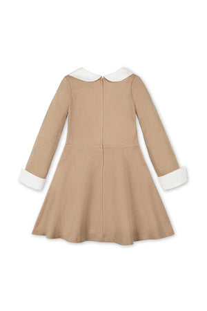 The image features a camel-colored dress for toddlers and girls, made from organic cotton. It showcases a classic silhouette with a Peter Pan collar and white cuffs.