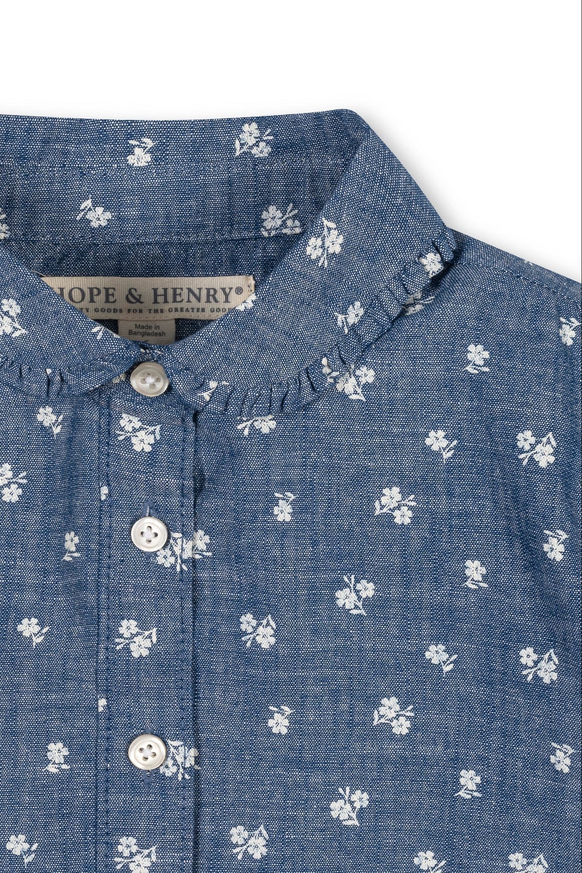 A close-up view of a chambray top featuring a Peter Pan collar, delicate floral patterns, and button details. Made from soft, sustainable organic cotton for toddlers and girls.
