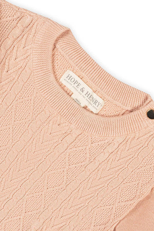 Close-up of a soft blush cable knit sweater dress from Hope & Henry, featuring intricate textured patterns and a classic round neckline, made from sustainable organic cotton for toddlers and.