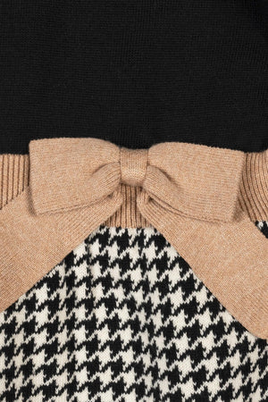 Close-up of a black houndstooth skater sweater dress featuring a solid black bodice, a decorative tan bow at the waist, and a soft organic cotton fabric, perfect for toddlers.