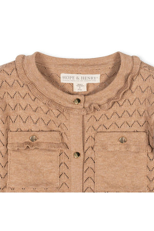 Close-up of a tan pointelle cardigan featuring a ruffle trim and two front pockets. Made from 100% organic cotton, this garment by Hope & Henry is perfect for toddlers and.