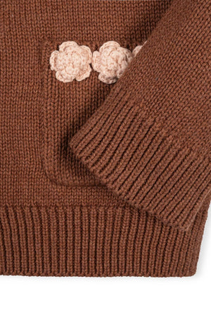 Close-up of a cinnamon-colored organic cotton cardigan featuring a textured knit and a decorative rosette pocket. The cozy design is perfect for toddlers and girls, emphasizing comfort and style.