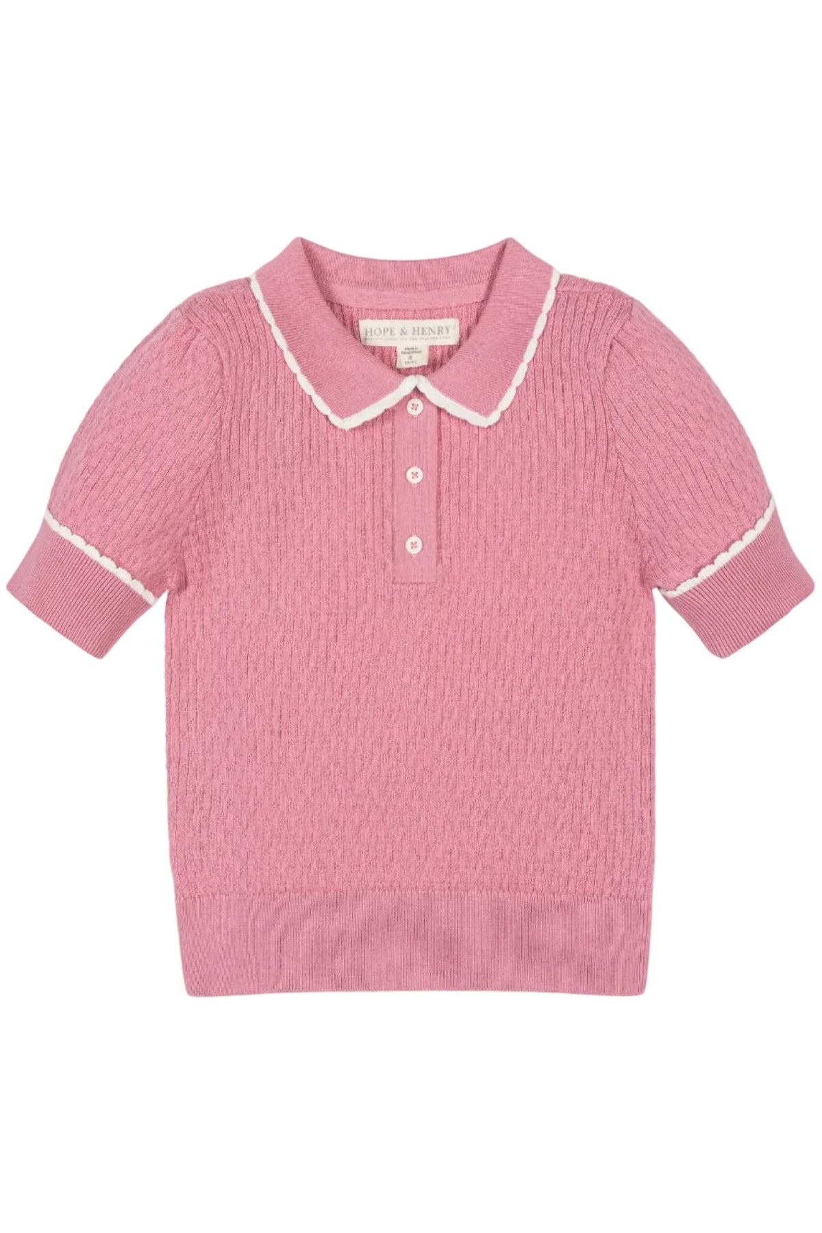 A soft pink short-sleeve sweater polo features a textured knit and a white-tipped Peter Pan collar. Made from organic cotton, it offers a stylish and sustainable choice for kids.