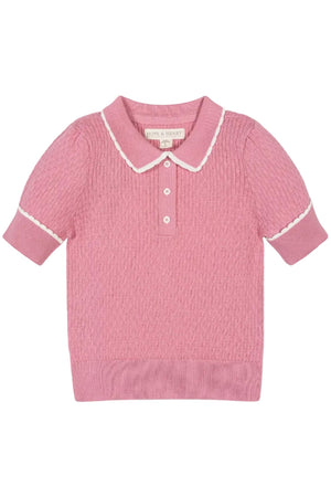 A soft pink short-sleeve sweater polo features a textured knit and a white-tipped Peter Pan collar. Made from organic cotton, it offers a stylish and sustainable choice for kids.