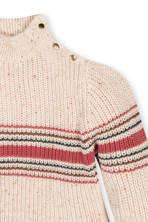 An ivory mock neck sweater features a textured knit with colorful stripes in red, black, and cream. The stylish design includes decorative buttons on the shoulder, perfect for kids.