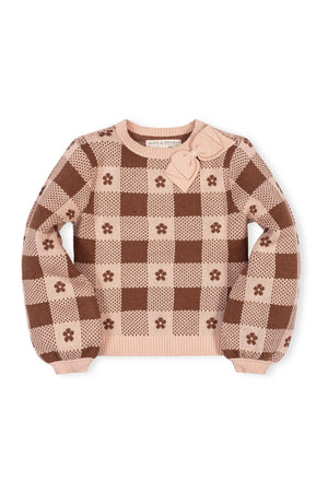 Light pink sweater featuring a checkered intarsia design in warm brown hues. The cozy garment includes a decorative bow detail and is made from soft, GOTS Certified organic cotton.