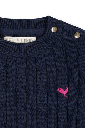Navy blue organic cotton cable knit sweater featuring gold buttons at the shoulder and a pink chicken logo. Designed by Hope & Henry, its perfect for toddlers and girls.