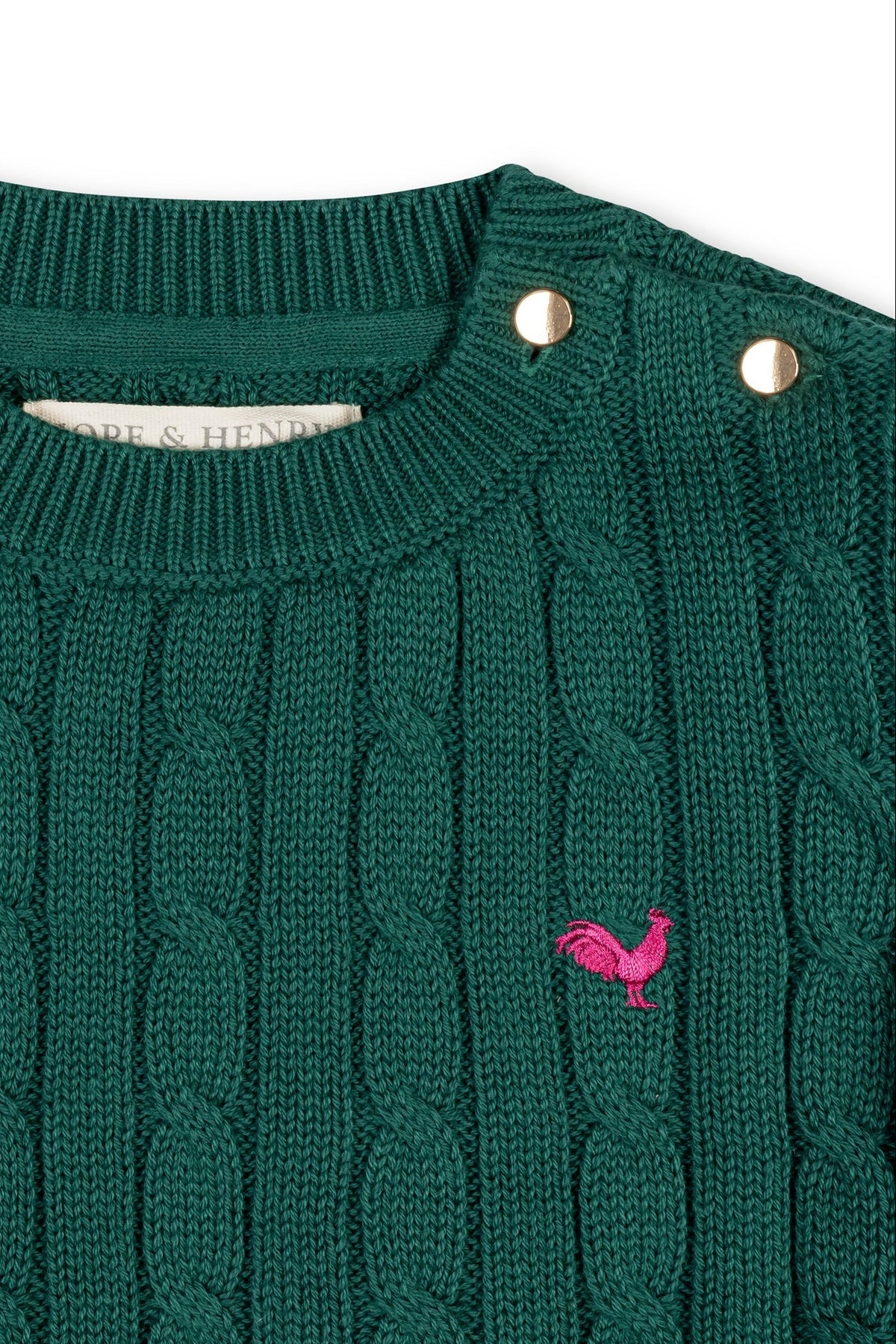 A green cable knit sweater featuring a round neckline and decorative buttons on one shoulder. It includes a small embroidered rooster logo, made from soft organic cotton for comfort.