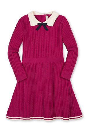 A vibrant fuchsia sweater dress features a cable knit design, scalloped white collar, and decorative navy bow. Made from organic cotton, it’s ideal for toddlers and girls special occasions.