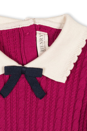 Close-up of a vibrant magenta sweater dress featuring a scalloped cream collar and a decorative navy bow. Made from soft organic cotton, it’s perfect for toddlers and girls.