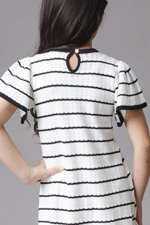 A girl models a black and white striped organic cotton sweater dress with short sleeves and a bow detail at the neckline, showcasing a button closure at the back.