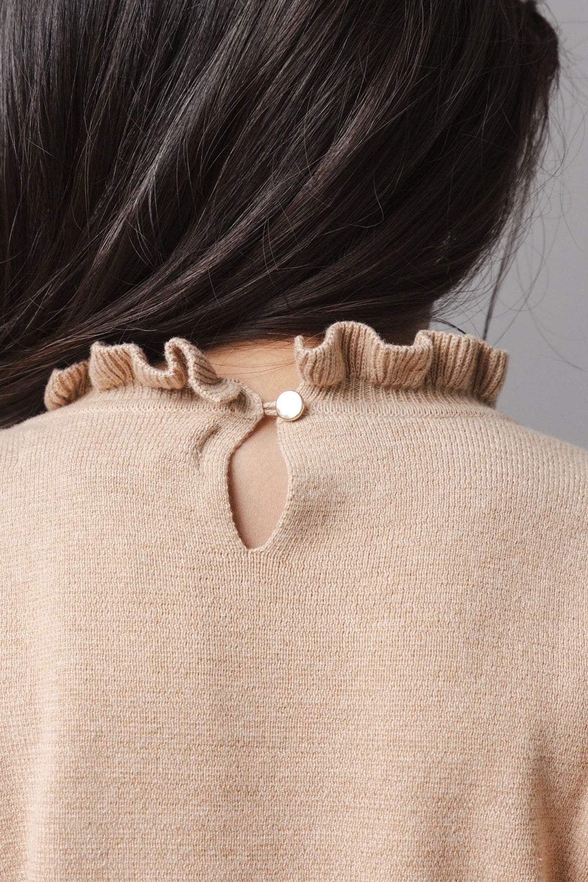 A close-up view of a toddlers camel-colored organic cotton sweater dress, featuring a ruffled neckline and a small button closure at the back. Soft and cozy for comfortable wear.