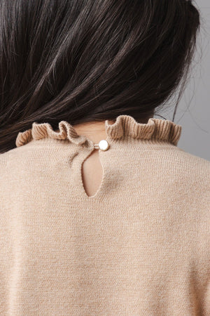 A close-up view of a toddlers camel-colored organic cotton sweater dress, featuring a ruffled neckline and a small button closure at the back. Soft and cozy for comfortable wear.