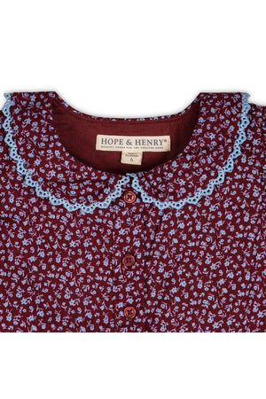 A close-up of a wine-colored dress featuring a Peter Pan collar with delicate blue crochet trim. The fabric showcases a floral pattern, and the brand label reads Hope & Henry.