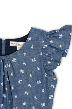 Close-up of a chambray dress featuring delicate white floral patterns and ruffle sleeves. The dress is made from soft organic cotton, designed for toddlers and girls, offering a stylish, comfortable.