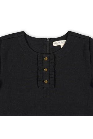 Close-up of a black organic cotton dress featuring a ruffle placket and three gold buttons. The soft fabric suggests comfort, making it suitable for toddlers and girls.