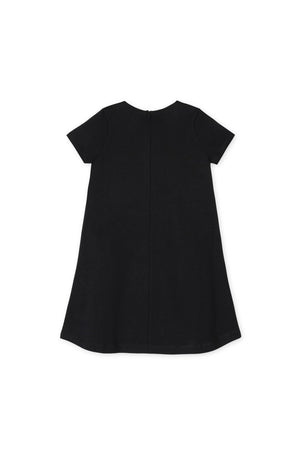 Back view of a black A-line dress with short sleeves and a ruffle placket. Made from organic cotton, this dress is designed for toddlers and girls, offering a timeless, comfortable.