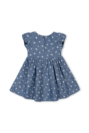 Back view of a soft blue chambray baby dress with smocked puff sleeves and delicate white floral embroidery, made from 100% organic cotton for comfort and sustainability.