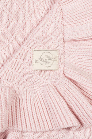 A pale pink, textured blanket featuring a delicate ruffle edge, with a label displaying HOPE & HENRY. Crafted from soft organic cotton, it offers a cozy and timeless look.