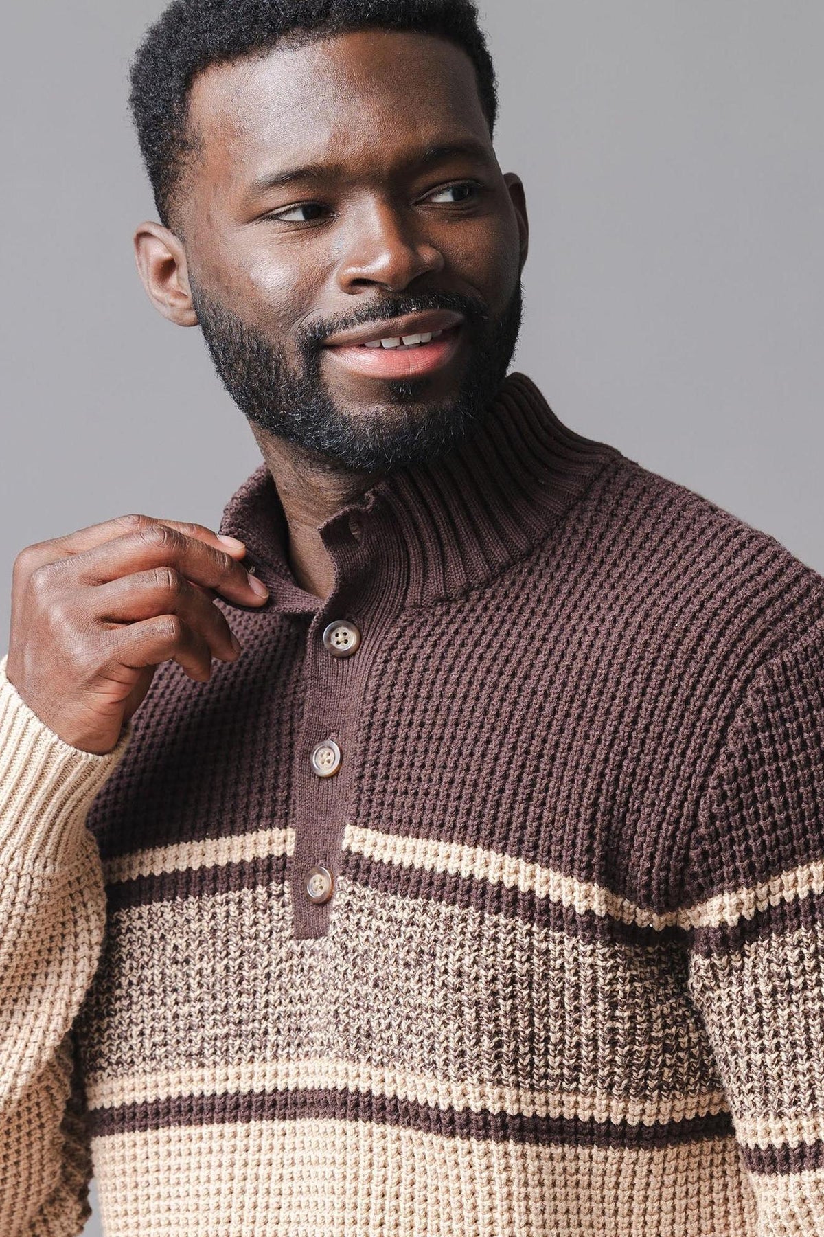 A man is wearing a stylish, mock neck waffle sweater featuring a brown and beige striped design.