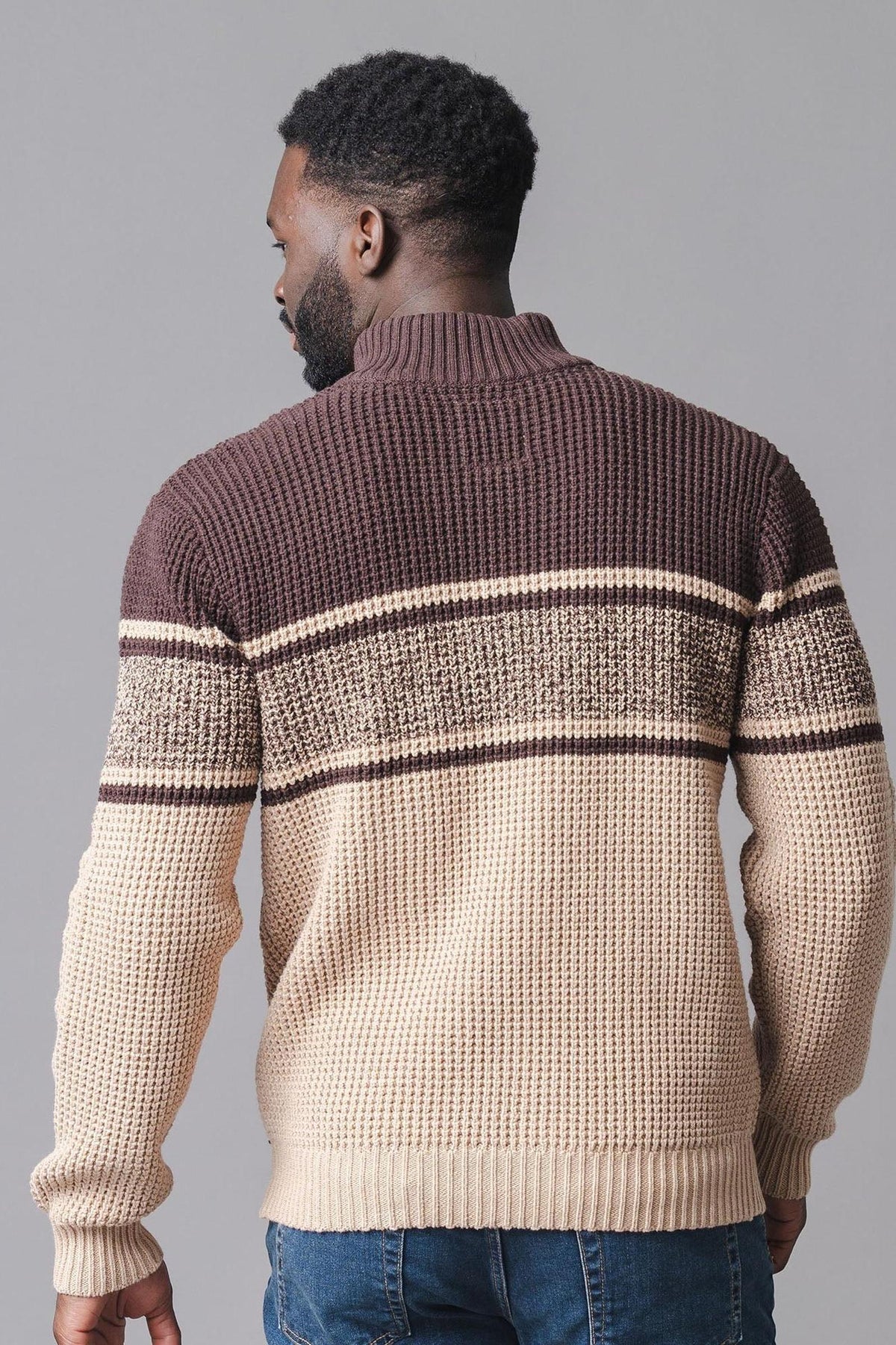 A man is seen from the back wearing a mock neck waffle sweater featuring a brown and cream striped design. The sweater is made from soft, organic cotton for comfort.