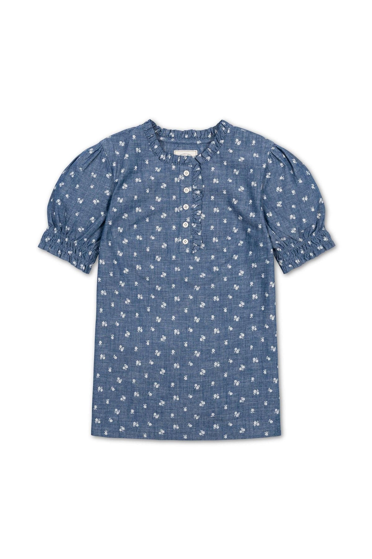 A blue chambray puff sleeve top features a delicate floral print, ruffle trim at the collar, and buttons down the front, crafted from 100% organic cotton for comfort.