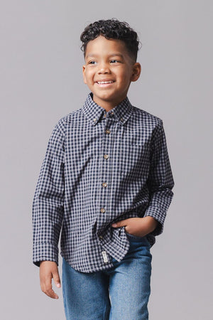 A young boy smiles while wearing a black gingham organic cotton poplin shirt with long sleeves and button-front closure, paired with blue jeans against a neutral background.