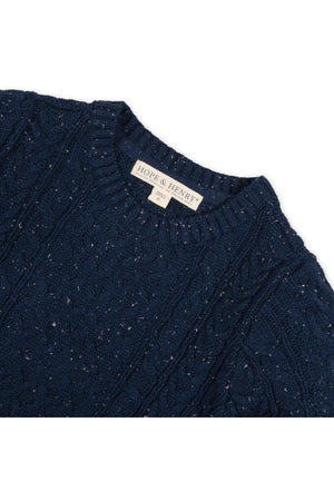 A close-up of a navy blue cable knit fisherman sweater from Hope & Henry, showcasing its textured pattern and organic cotton material. The label is visible at the neckline.