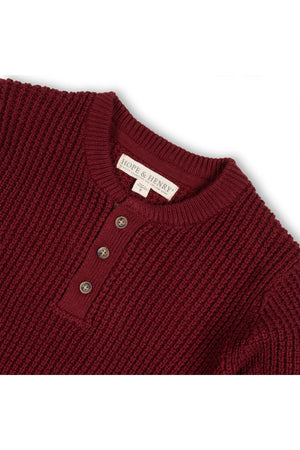 A close-up of a burgundy waffle-knit sweater henley featuring a three-button placket and ribbed collar. Made from soft organic cotton, it is designed for comfort and style.