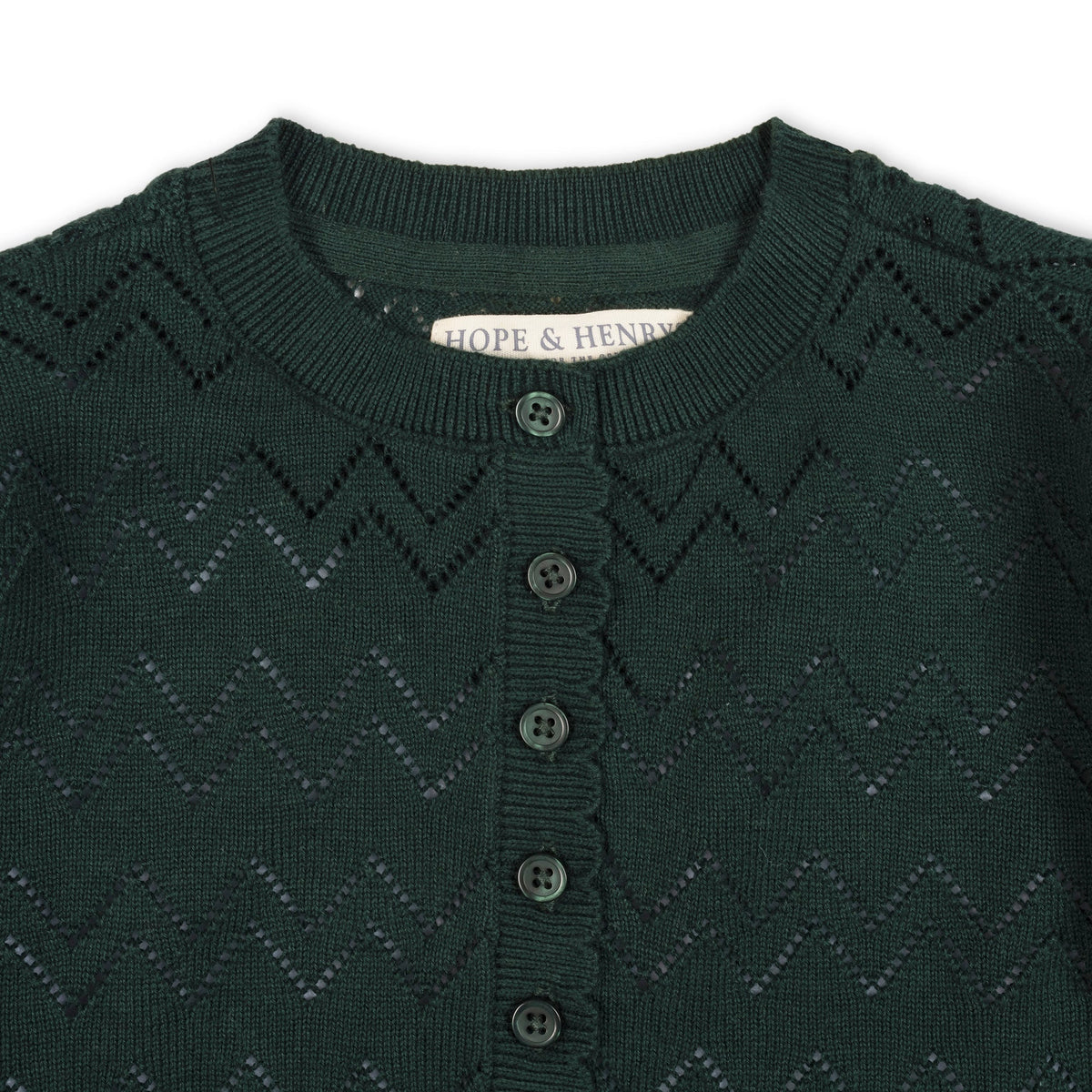 Close-up of a deep green organic cotton henley sweater featuring a scalloped placket and textured zigzag pattern, with button closures and the brand label Hope & Henry visible.