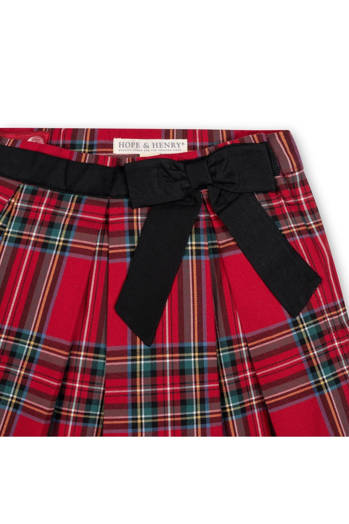 Close-up of a red holiday tartan pleated skirt featuring a black waist sash with a bow. The skirt is made from soft organic cotton, suitable for toddlers and girls.