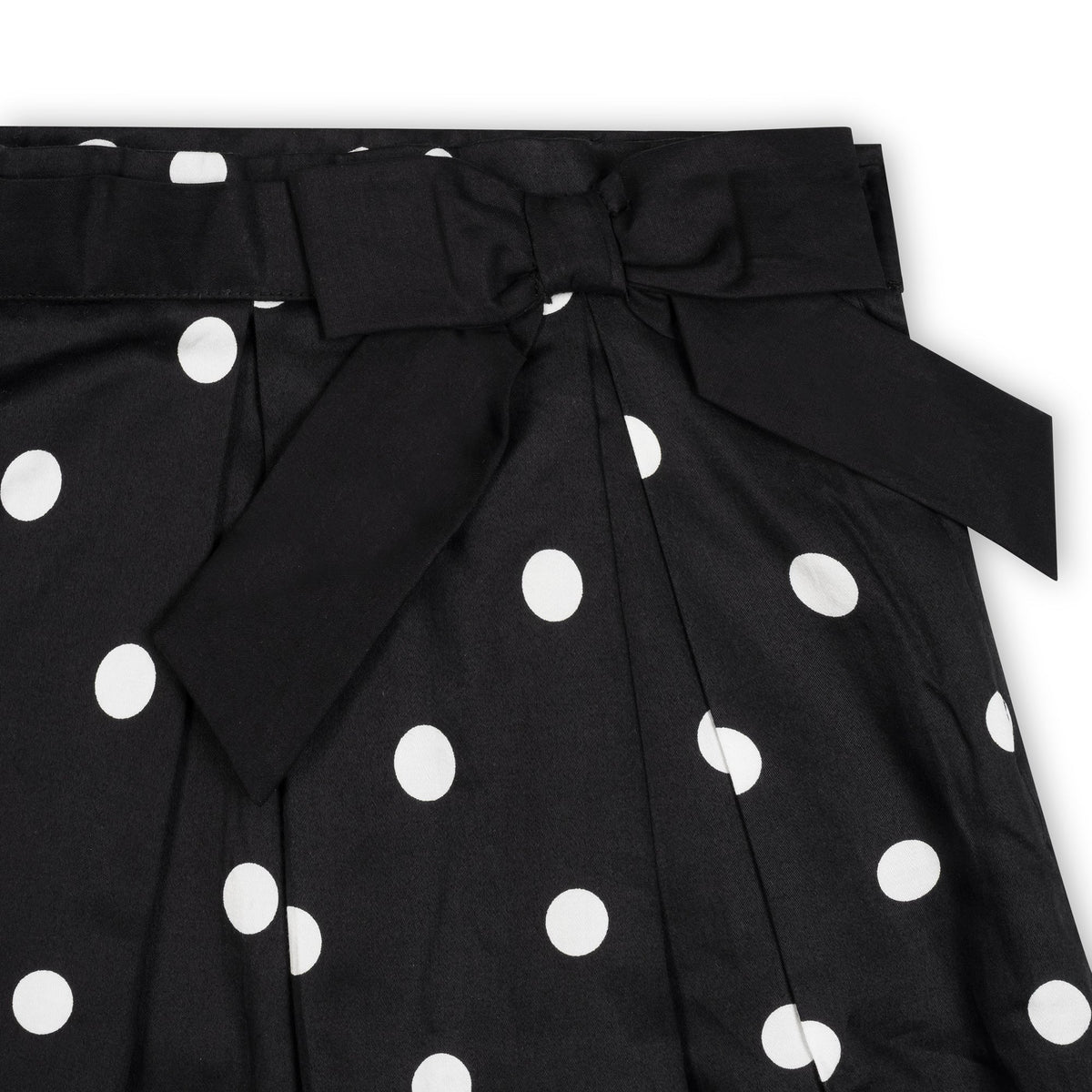 Close-up of a black pleated party skirt featuring white polka dots and a large bow at the waist. Made from soft organic cotton, it is designed for toddlers and girls.