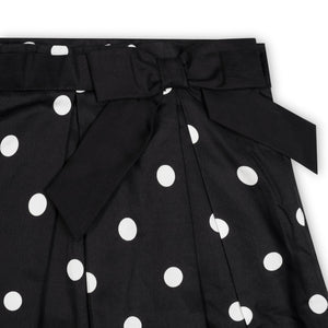 Close-up of a black pleated party skirt featuring white polka dots and a large bow at the waist. Made from soft organic cotton, it is designed for toddlers and girls.
