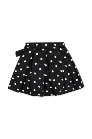 A black pleated party skirt featuring white polka dots, crafted from soft organic cotton. The skirt includes a waist sash with a bow, suitable for toddlers and girls.