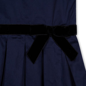 Close-up of a navy blue dress featuring a soft texture, a velvet waist sash with a bow, and pleated detailing. Made from organic cotton, perfect for toddlers and kids.