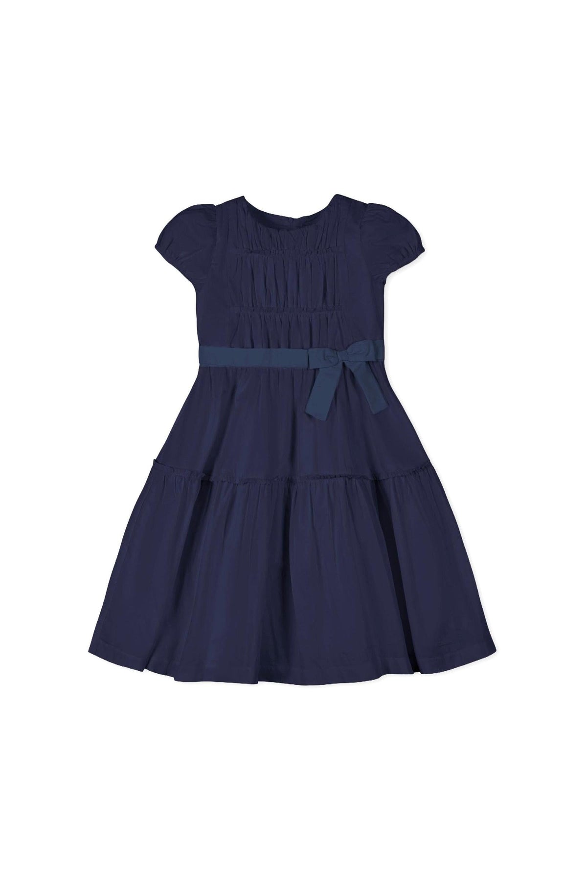 A navy organic cotton tiered party dress featuring puff sleeves and a shirred bodice. It includes a bow detail at the waist, perfect for toddlers and girls.