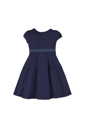 Navy organic cotton puff sleeve dress featuring a tiered skirt and waist sash. The back has a zipper for easy dressing, perfect for toddlers and girls at special occasions.